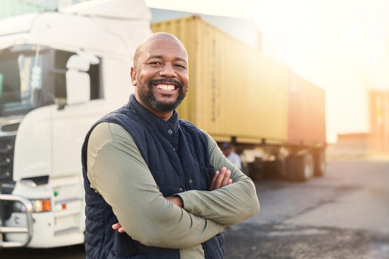 Man, portrait and arms crossed by truck, container stack and happy for transport job. Driver, smile and shipping cargo freight with happiness in transportation service, stock delivery or supply chain.